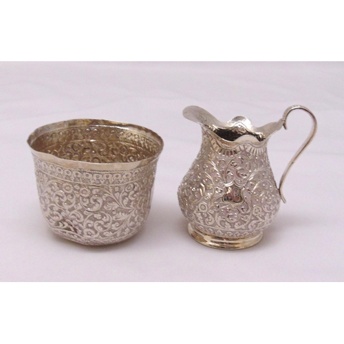 438 - An Indian white metal pear shaped cream jug profusely chased with flowers and leaves and a matching ... 