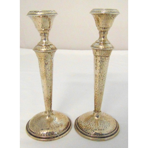 302 - A pair of hallmarked silver hand hammered table candlesticks tapering cylindrical stems on raised ci... 