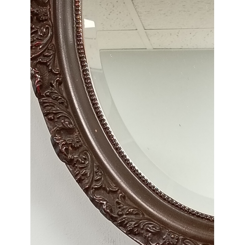 484 - Oval bevelled mirror in brown scrolled detail frame H 49cm x W 38cm