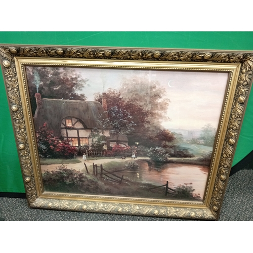 558 - Ornate framed print of a cottage by the river with children and dog. H 58CM x W 69cm