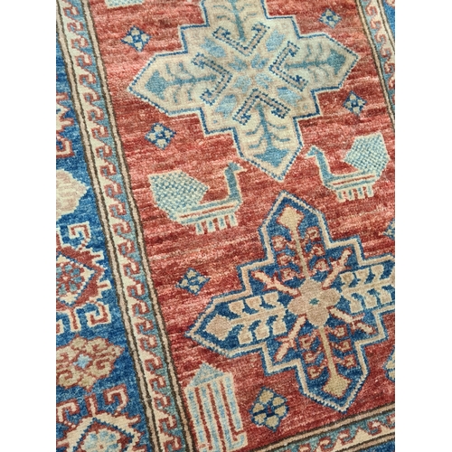 501 - Vintage Brick Red & Blue Patterned Persian/ Kazak Rug. Measures 100cm x 60cm.