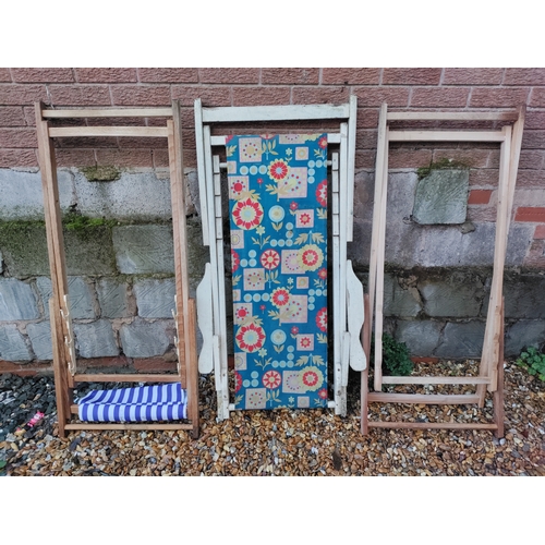 82 - A collection of three wooden deck chairs - two are just frames and the third features a floral desig... 