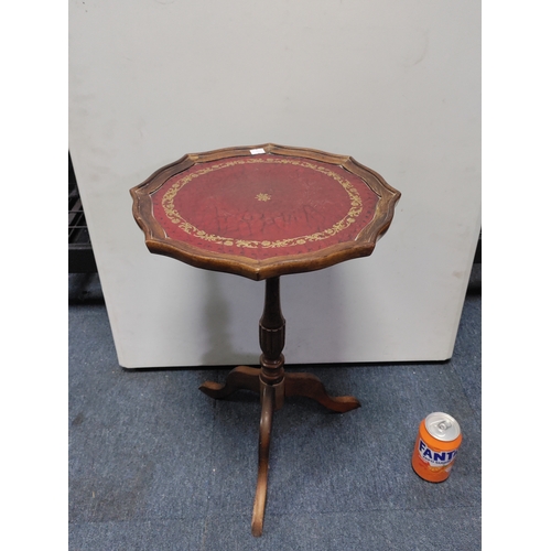 133 - A vintage wood side table with a pie-crust edge and red leather top with gold leaf pattern inlay.