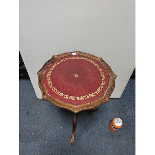 133 - A vintage wood side table with a pie-crust edge and red leather top with gold leaf pattern inlay.
