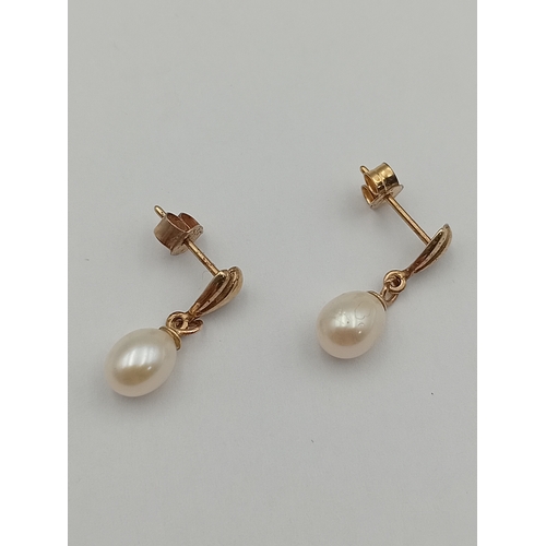 100 - A pair of tested gold dangle earrings set with pearls.