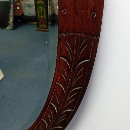 116 - Oval wall mirror in stained hardwood frame, the border carved with stylised foliate panels and oval ... 