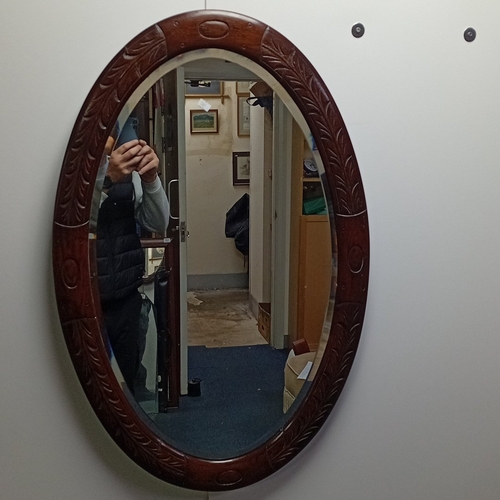 116 - Oval wall mirror in stained hardwood frame, the border carved with stylised foliate panels and oval ... 