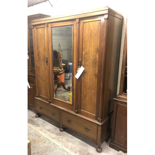 345 - A large three door wooden wardrobe, with built-in central mirror panel (43cm x 121cm) on four rounde... 