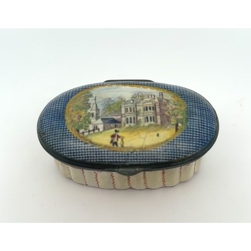 63 - An oval enamel pill/ patch box, probably Bilston with fluted body and painted lid depicting a church... 