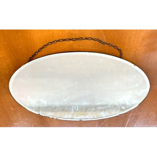 312 - A frameless oval shaped wall mirror, wooden backed with the glass held via four clasps. Chain hangin... 