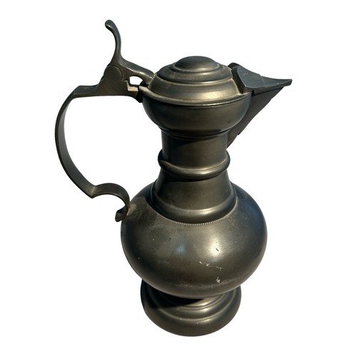 23 - Pewter lidded jug (height 26cm) with two-sided religious token (possibly lead) 6cm x 5cm.