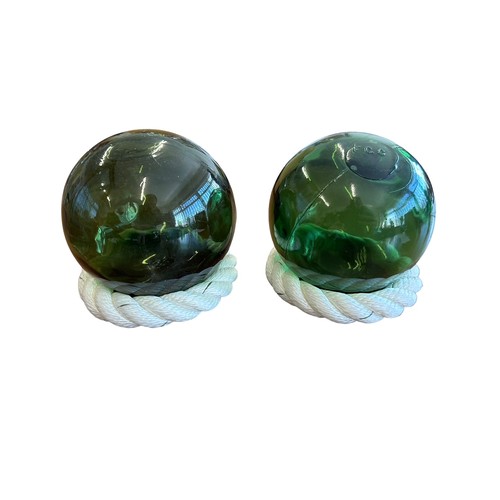 110 - Pair of hand blown green glass fishing floats (buoys), each on rope stand.