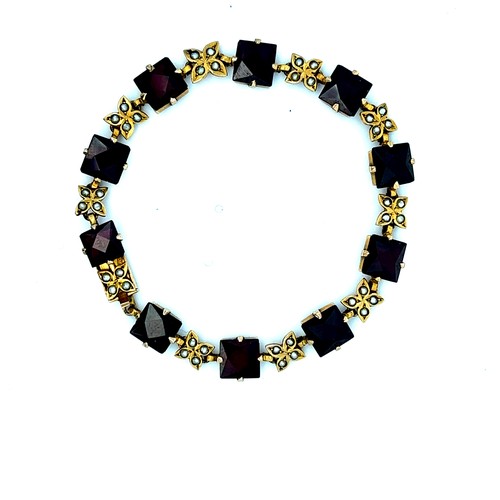 37 - A yellow metal bracelet set with 10 square cut garnets interspersed with flower shaped links each se... 