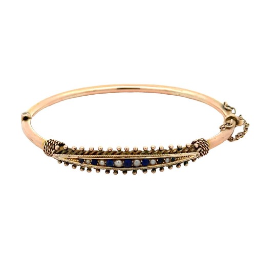 69 - An unmarked 9ct gold hinged bangle. Bangle is set with blue stones and pearls and has rope twist and... 