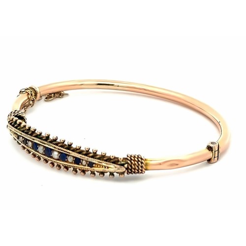 69 - An unmarked 9ct gold hinged bangle. Bangle is set with blue stones and pearls and has rope twist and... 