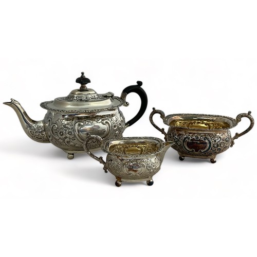 202 - A matching sterling silver teapot with ornate repousse decoration, on four ball feet and  ebonised f... 