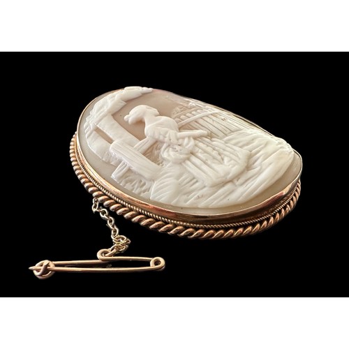 18 - A gold shell cameo brooch depicting a lady looking over a fence to a house beyond. With rope twist s... 