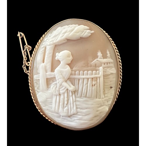 18 - A gold shell cameo brooch depicting a lady looking over a fence to a house beyond. With rope twist s... 