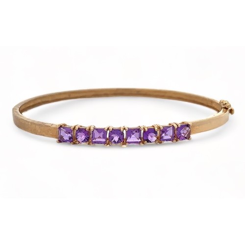 8 - A small 9ct gold hinged bangle set with eight purple gemstones, likely CZs,  alternating square cut ... 