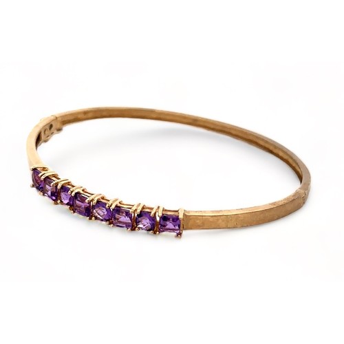 8 - A small 9ct gold hinged bangle set with eight purple gemstones, likely CZs,  alternating square cut ... 