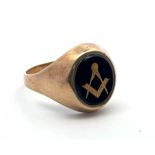 12 - A 9ct gold signet ring with black oval onyx decorated with gilt Masonic square and compass. Size . W... 