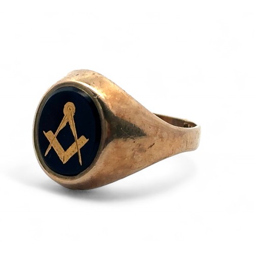 12 - A 9ct gold signet ring with black oval onyx decorated with gilt Masonic square and compass. Size . W... 