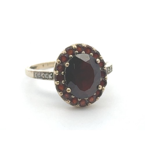 64 - A red and white stone cluster ring, stamped 9k. Oval dark red paste centre stone surrounded by small... 