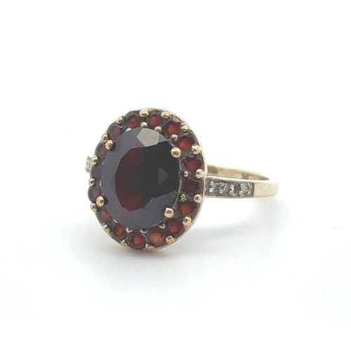 64 - A red and white stone cluster ring, stamped 9k. Oval dark red paste centre stone surrounded by small... 