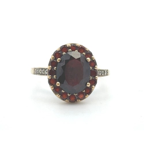 64 - A red and white stone cluster ring, stamped 9k. Oval dark red paste centre stone surrounded by small... 