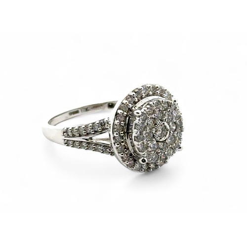 76 - A diamond cluster ring set in 9ct white gold with split shoulders. Inscribed to inner shank as 1ct o... 