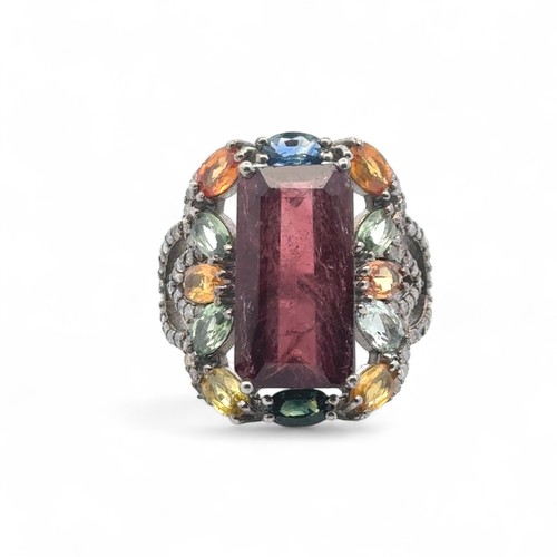 56 - A large silver dress ring set with step cut tourmaline, surrounded by multi coloured sapphires and d... 