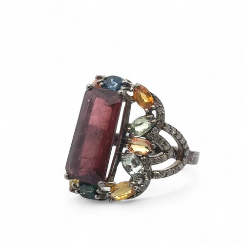 56 - A large silver dress ring set with step cut tourmaline, surrounded by multi coloured sapphires and d... 