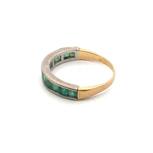 12 - A channel set emerald ring in a yellow metal mount, stamped 18. Size N. 2.95g.