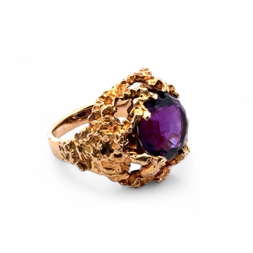 1 - A textured gold ring set with a round step cut amethyst  (12mm diameter), stamped 9ct. Size K. Weigh... 