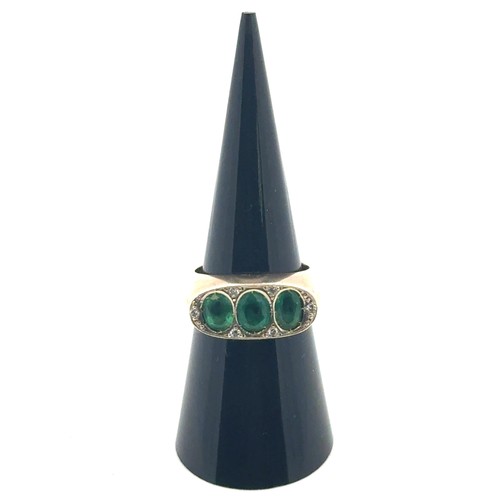 3 - A three stone emerald ring with diamond, size M. Emeralds each approx 6mm x 5mm. Unmarked yellow met... 