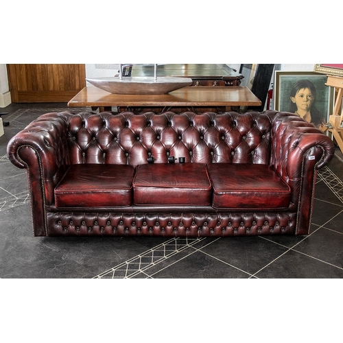 1031 - Three Seater Chesterfield Sofa, covered in a burgundy leather and supported on castors. Fully button... 