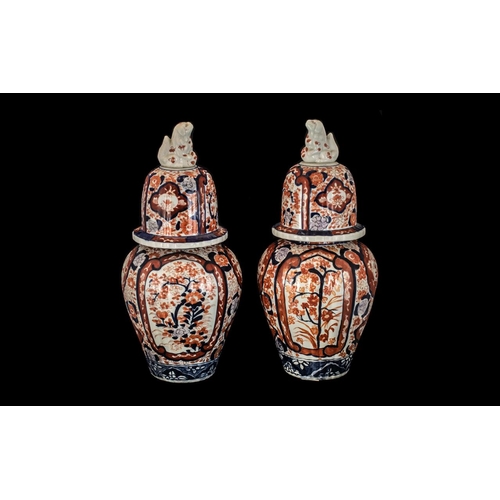 832 - Two Imari Jars and Covers of typical form, the covers surmounted by Foo Dogs, iron red and blue deco... 