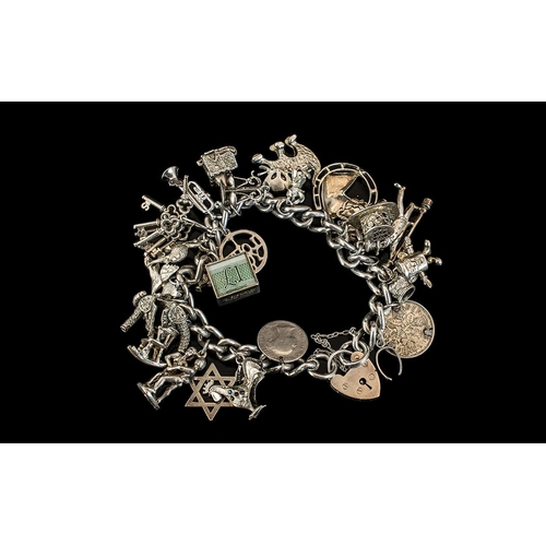 149 - A Silver Charm Bracelet with padlock fastener, loaded with 20+ charms. Gross weight 85 grams.