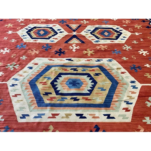 1059 - An Aztec Design Woolen Rug, Red Salmon Ground, Geometric Blue And White Border, 310 x 255 cm.