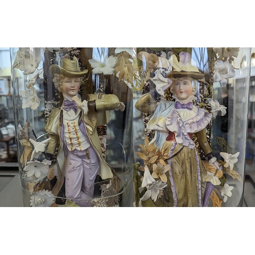 601 - Pair of Victorian Bisque Figures inside glass domes, a traditional lady and gentleman surrounded by ... 