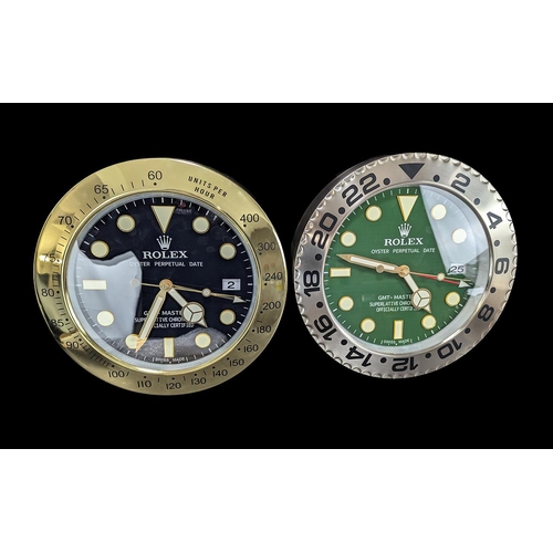 1103 - Two Rolex Style Dealer Display Wall Clocks, comprising one with a green face, date aperture, metal s... 