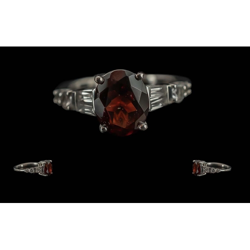 257 - Red Garnet Solitaire Style Ring, a 4.25ct oval cut garnet solitaire, accented by two tapered baguett... 