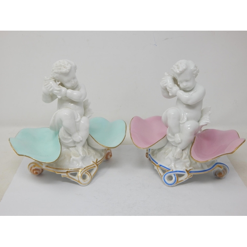 A Pair of Large Antique Figural Table Salts with Blue Crossed Swords Marks to Bases: Both with Central Blanc de Chine Putti Listening to Seashells Between Pink & Teal Glazed Shell Shaped Salts on Rococo Bases: Each Measuring 15cm wide x 14.5cm high