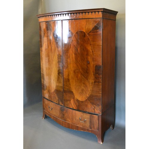 439 - An Edwardian mahogany bow fronted wardrobe, the moulded cornice above two oval inlaid doors above a ... 