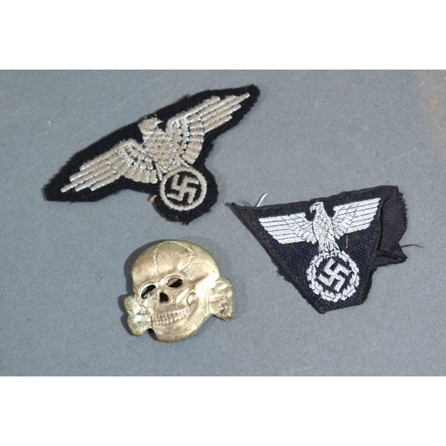 405 - A Second World War German SS Cap Badge in the form of a skull together with two SS cloth badges