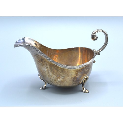 216 - A Sheffield Silver Sauce Jug with scroll handle upon three shaped feet retailed by Walker & Hall 5 o... 