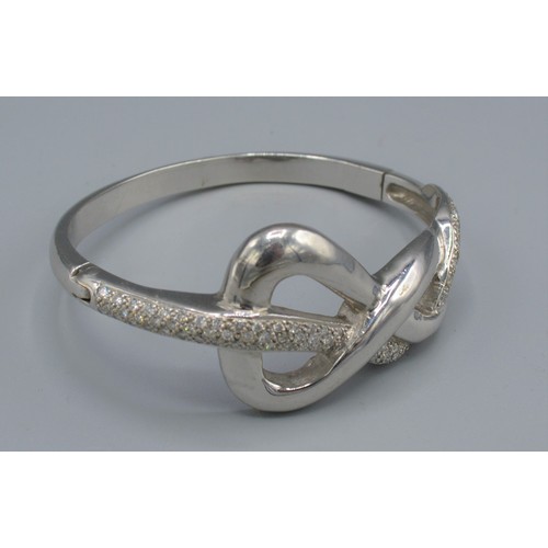 84 - An 18ct white gold diamond set bangle of shaped scroll form, set with lines of diamonds, 71.7 grams,... 