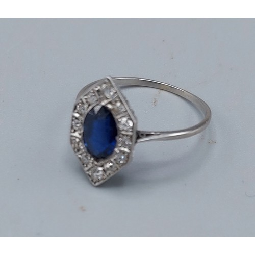 144 - An Art Deco white metal ring set with a central Sapphire surrounded by Diamonds of hexagonal form, 2... 