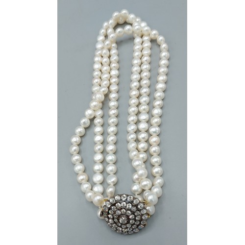 149 - A triple row pearl choker, the large clasp set with a central Diamond surrounded by three tiers of D... 