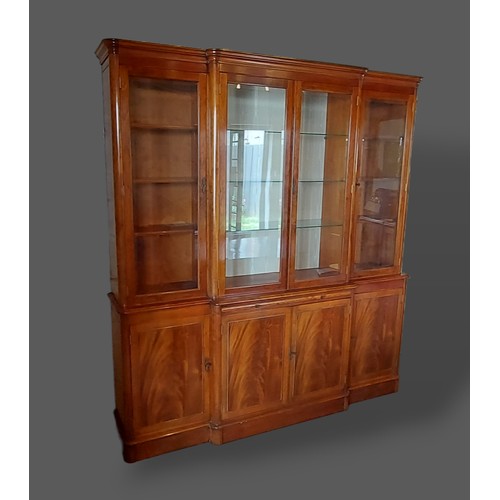 435 - A mahogany breakfront bookcase retailed by Harrods with a moulded cornice above four glazed doors en... 